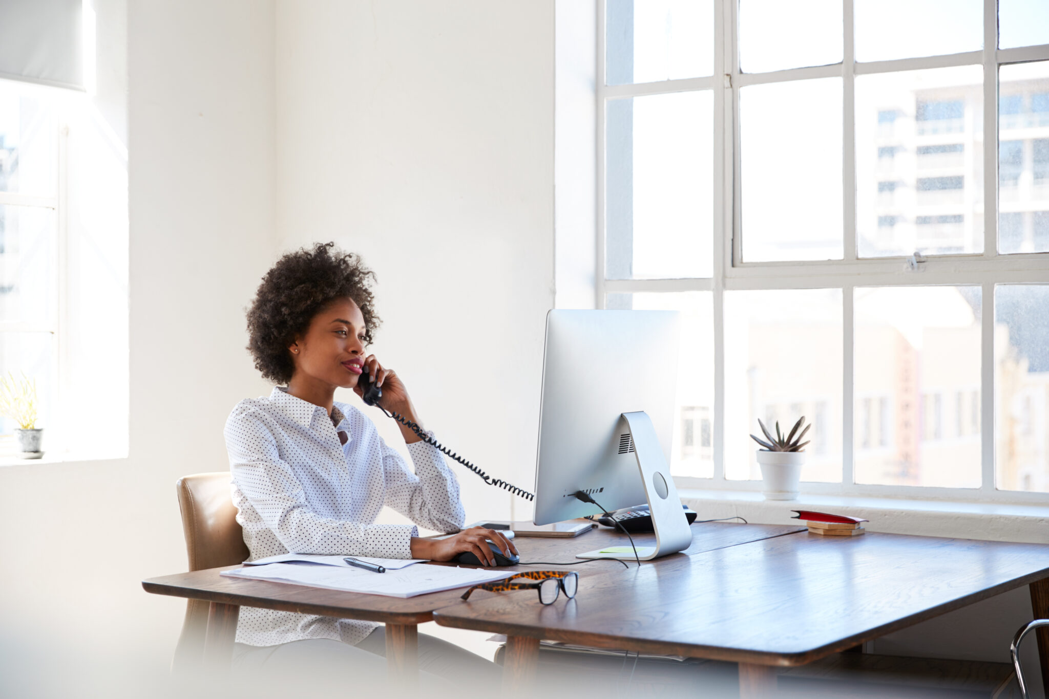 Young,Black,Woman,Talking,On,Phone,At,Her,Desk,In