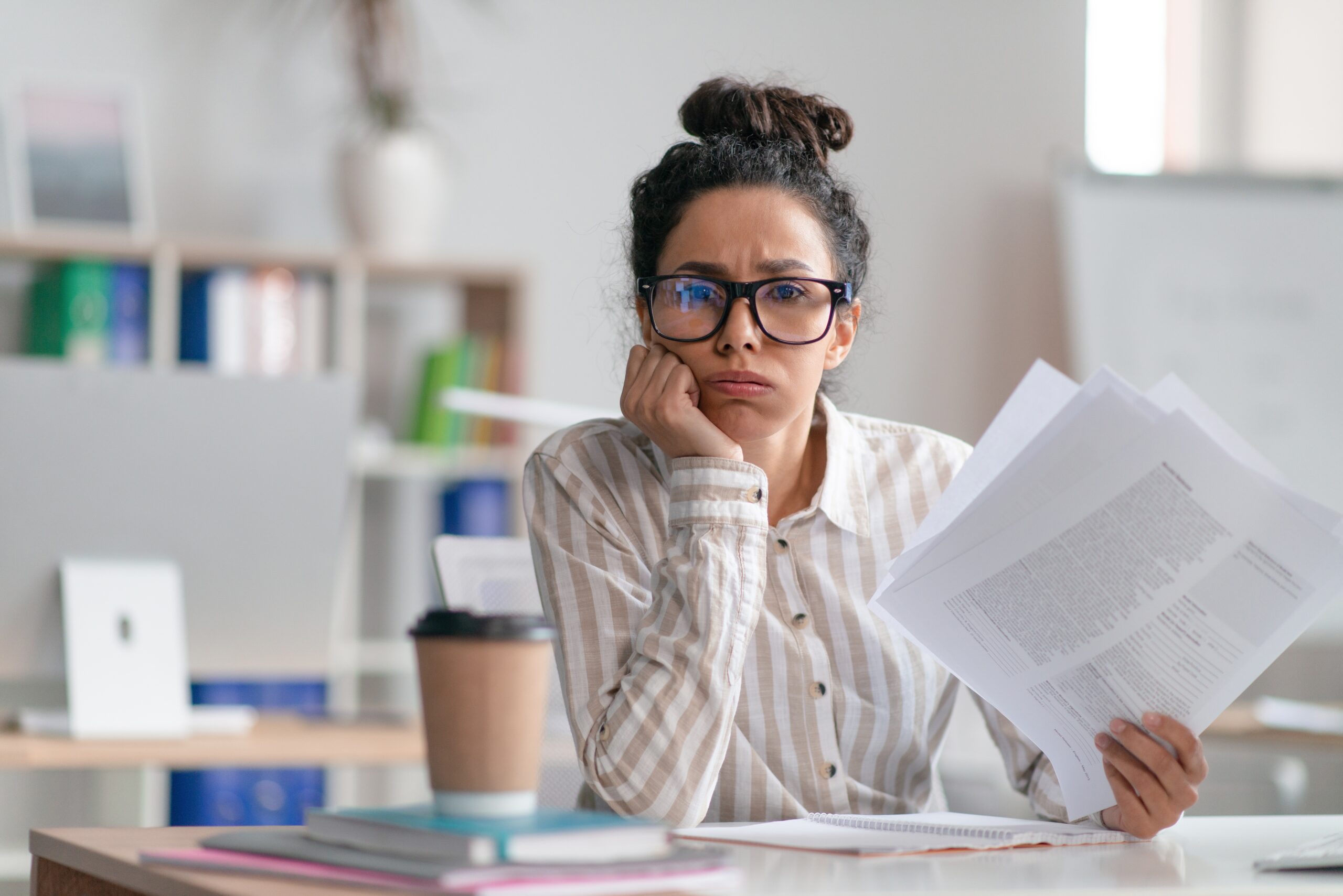 Tired,Female,Office,Worker,Looking,At,Camera,And,Holding,Documents,